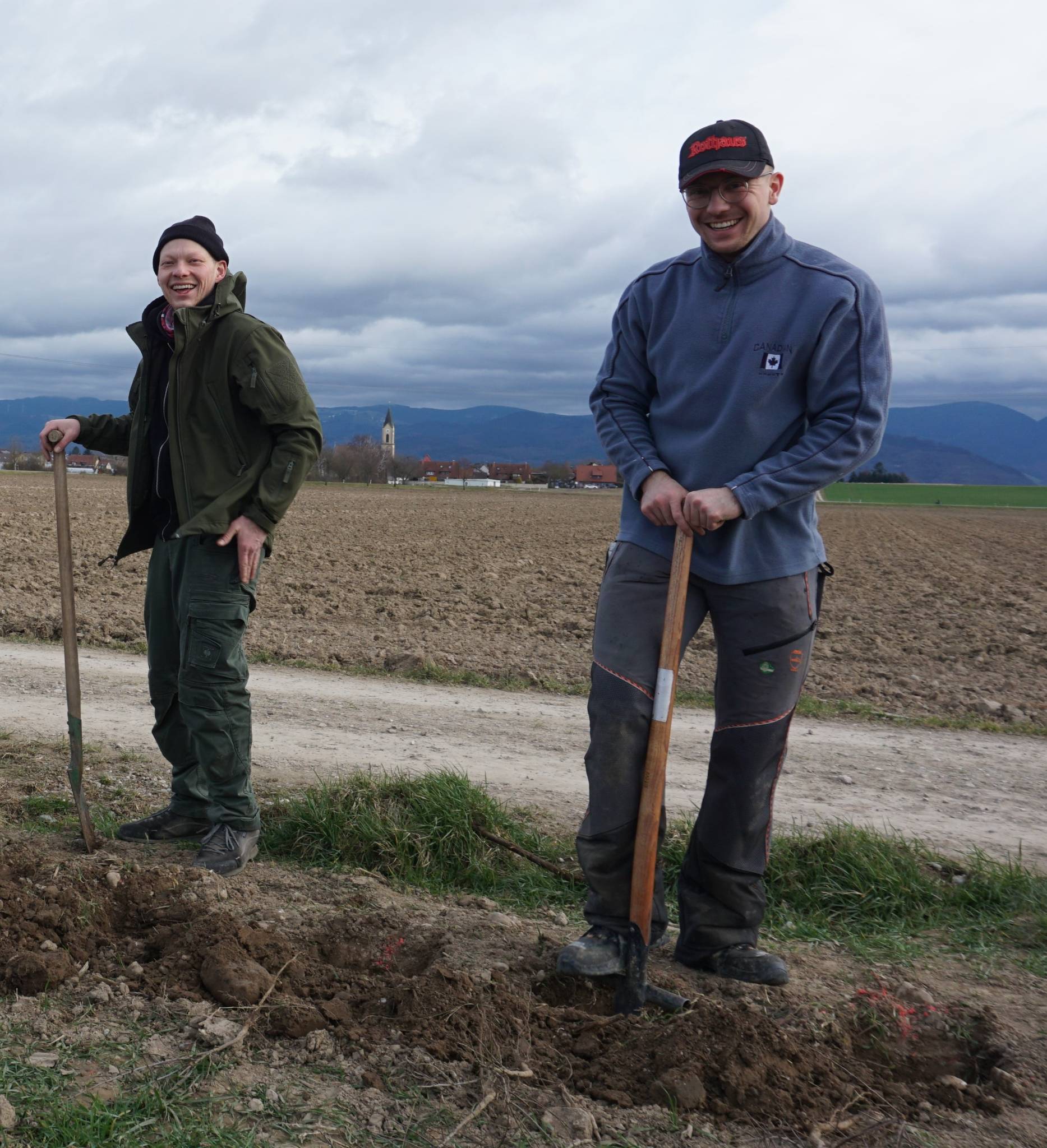 Two people with shovels beside a plowed field